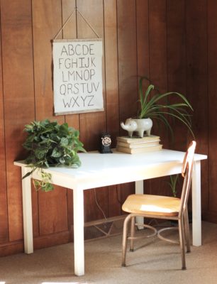 homemade canvas alphabet sign hanging above a white wooden kids desk with an old school chair