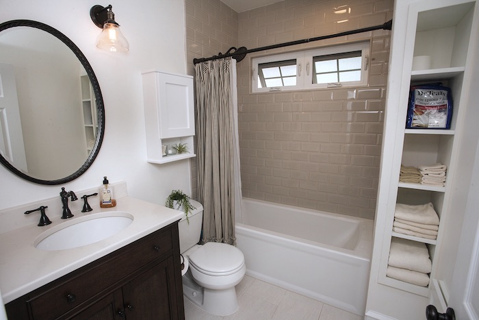 Small bathroom remodel with built in shelves next to shower and laundry shute for unique storage solutions.