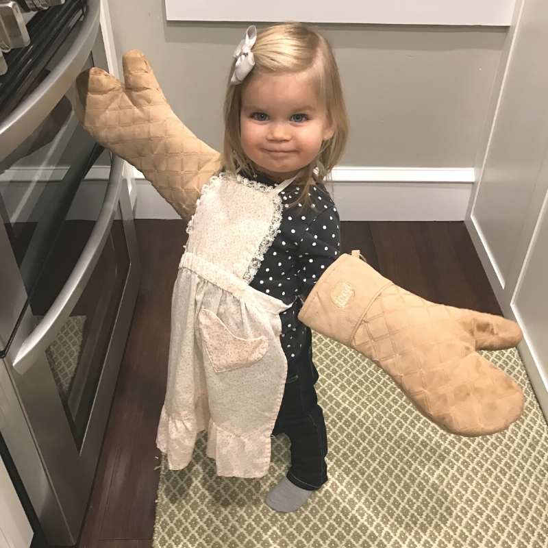 little girl with an apron and oven mitts
