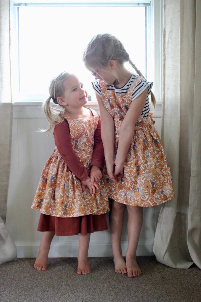 two little girl's in matching pinafore aprons