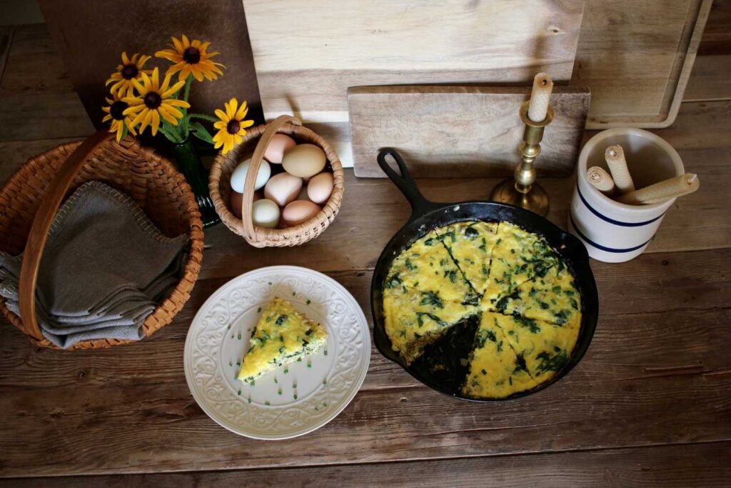 Cast iron skillet frittata, fresh eggs and cloth napkins in vintage baskets and rolled beeswax candles in a crock.