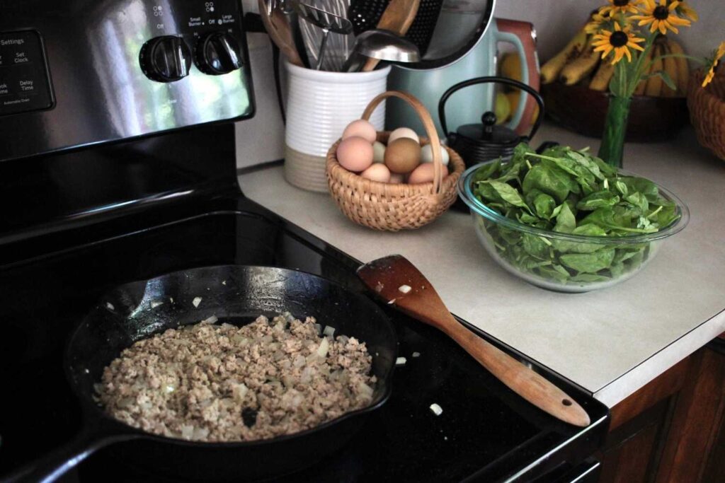 Ground turkey sausage in a cast iron skillet with fresh eggs in a basket and spinach in a bowl.