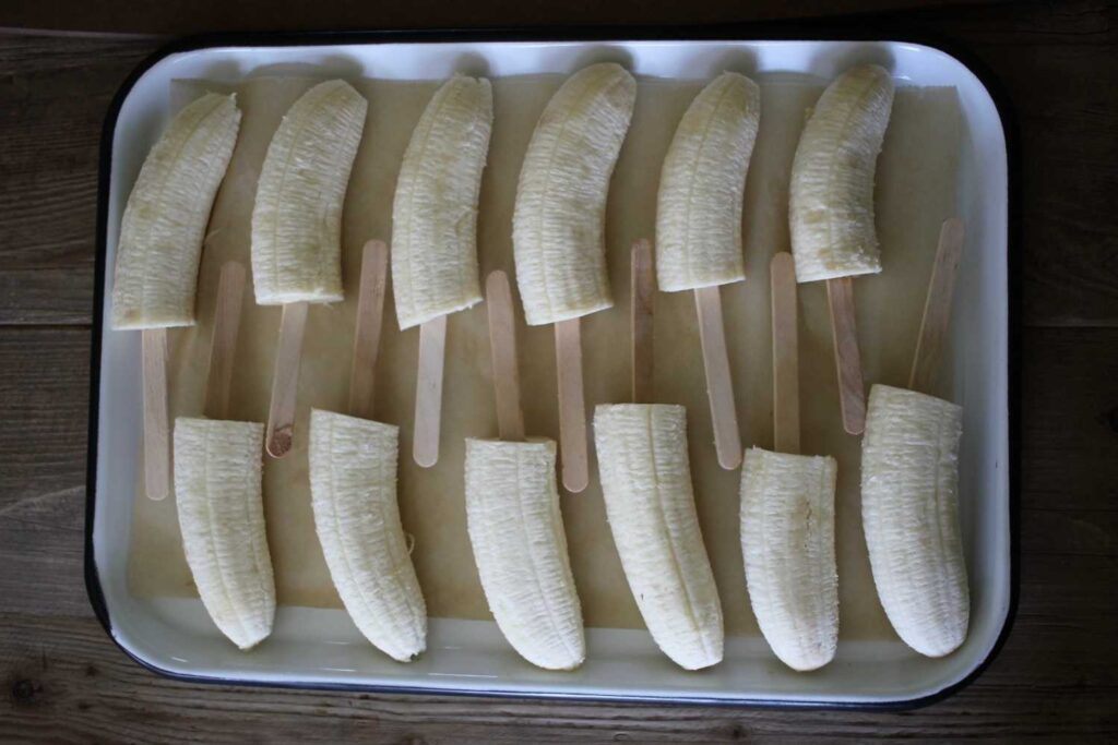 a tray of bananas cut in half with popsicles stuck in the bottom