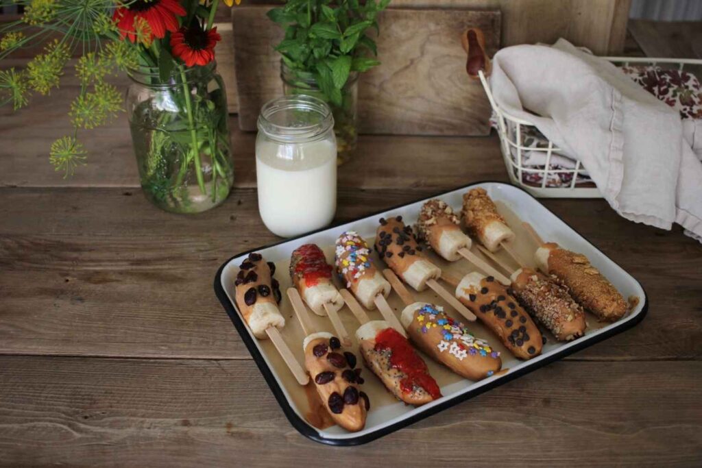 a summer treat snack of frozen bananas with nut butter and toppings a glass of milk and flowers.
