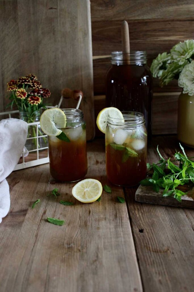 Two cold refreshing drink with mint and lemon laying on the table, fresh cut flowers in the background. 