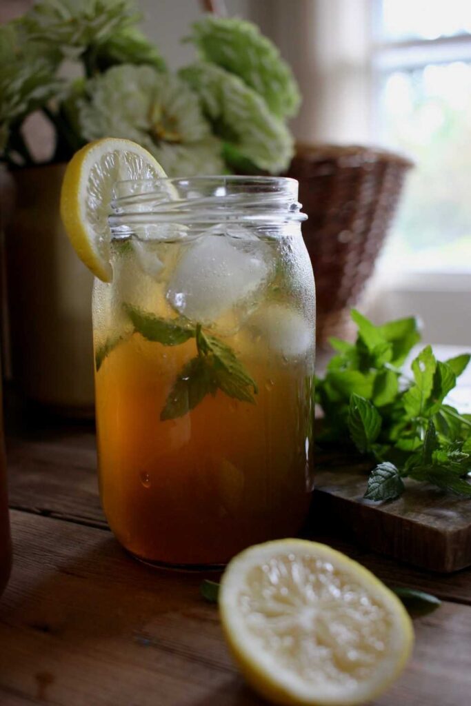 Natural sweetened herbal iced tea with condensation on the glass and fresh mint and lemon on the table.