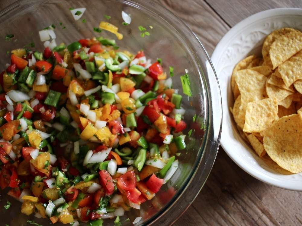 Homemade fresh salsa in a large clear pyrex bowl next to a cream bowl filled with corn chips.