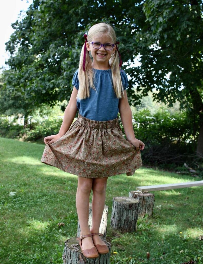 Young girl wearing a homemade elastic waist skirt while standing on a log stump.