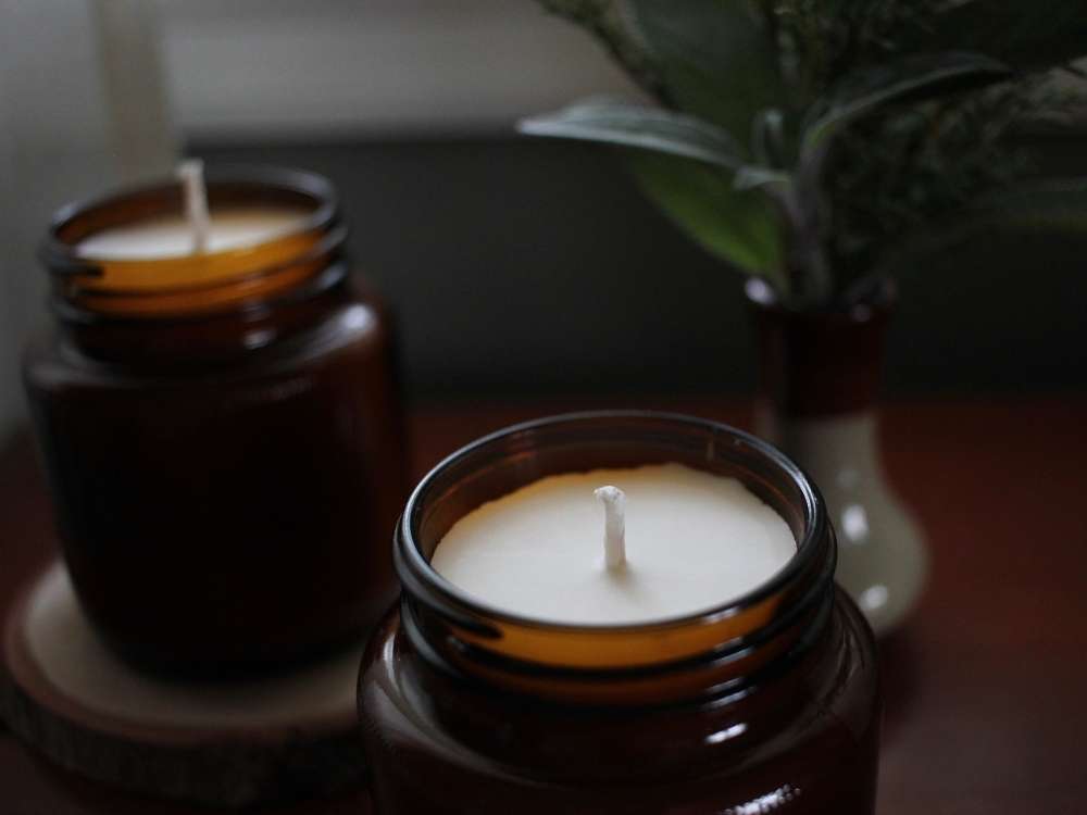 A close up of a homemade soy candle with a small vase of greens and another soy candle in the background.
