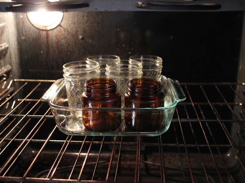 Six glass jars placed in the oven in a dish to warm up.