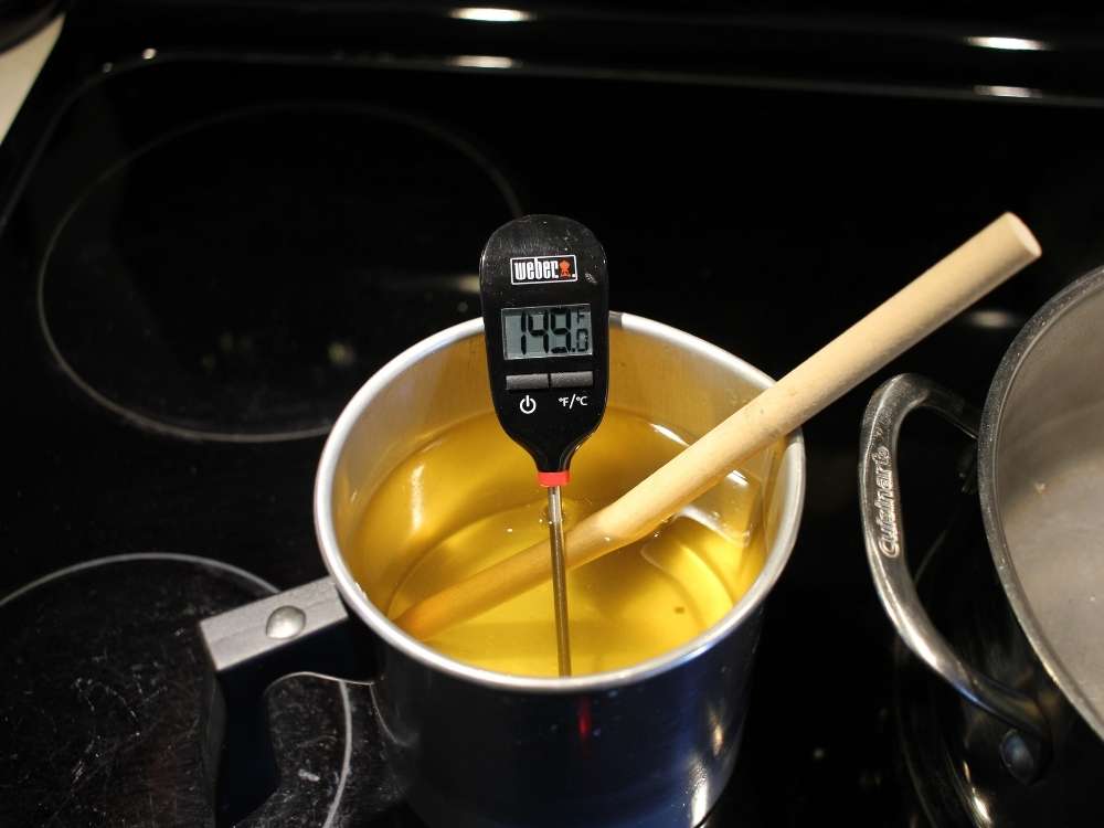 A thermometer reading 149F placed in a pouring pot of melted soy wax.