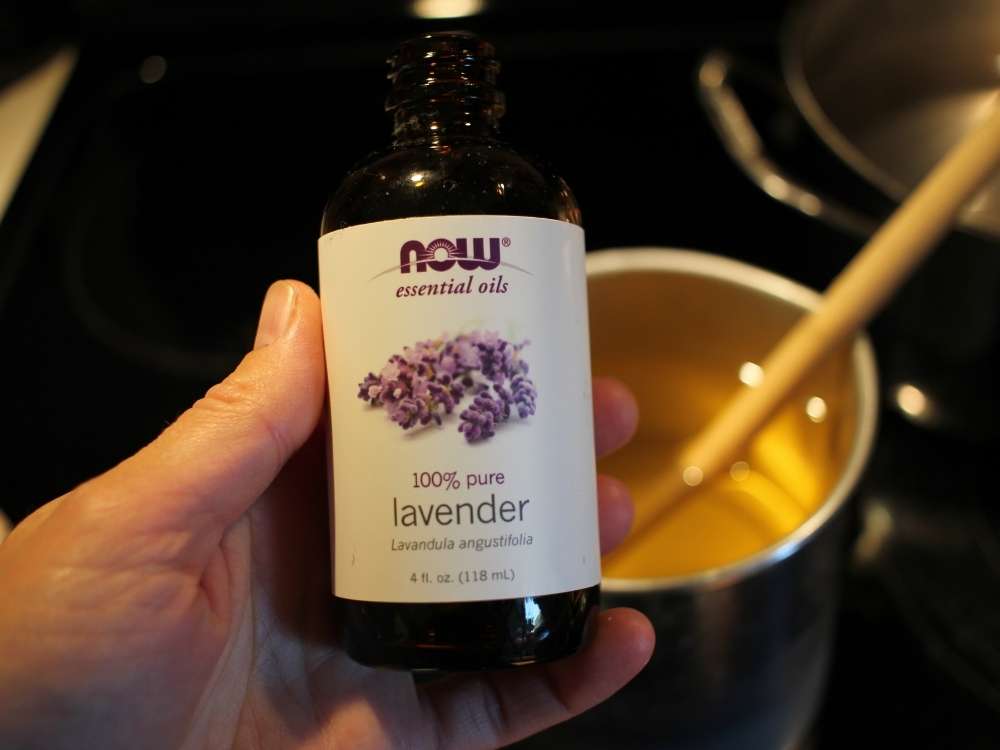 A women's hand holding a bottle of lavender essential oil with melted soy wax in the background.