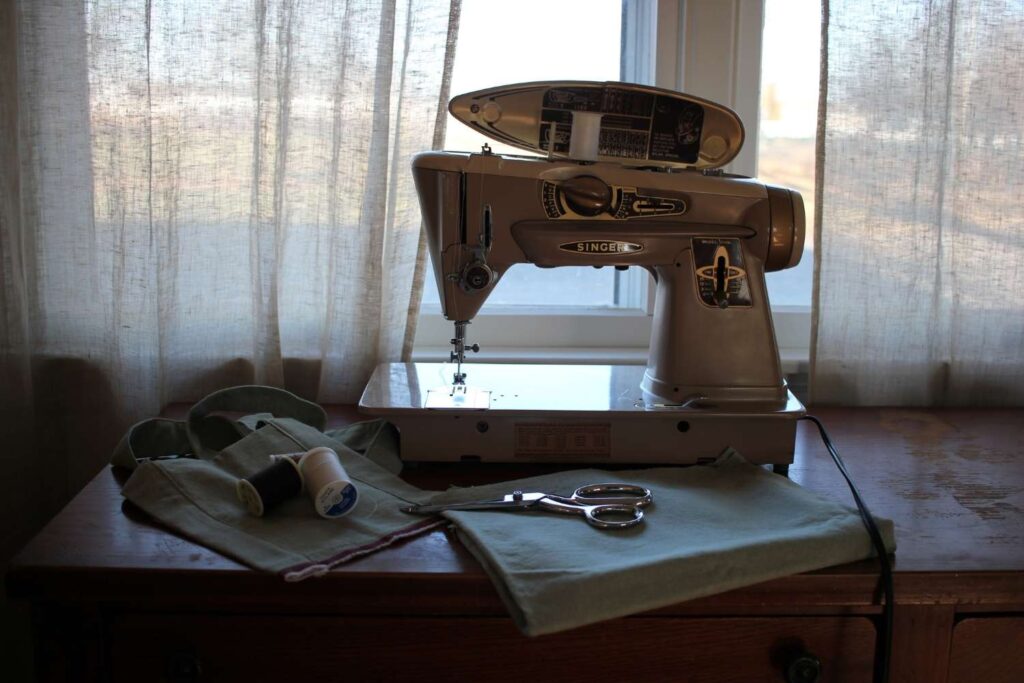 An antique singer sewing machine with a sewing project sitting on a desk.