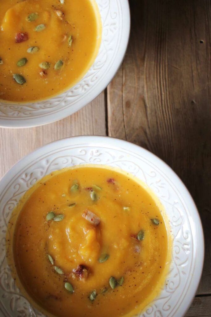 An up close image of thick butternut squash soup with bacon and pumpkin seeds and fine ground black pepper sprinkled on top.