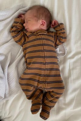 Newborn baby in a striped sleeper laying with arm stretched above head