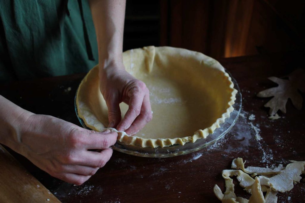 Close up of woman's hand crimping the edges of the pie crust.