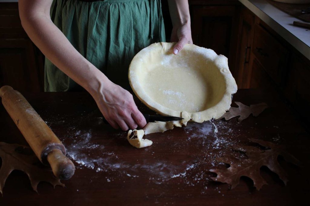 Close up of woman cutting edge of pie crust off with a knife.