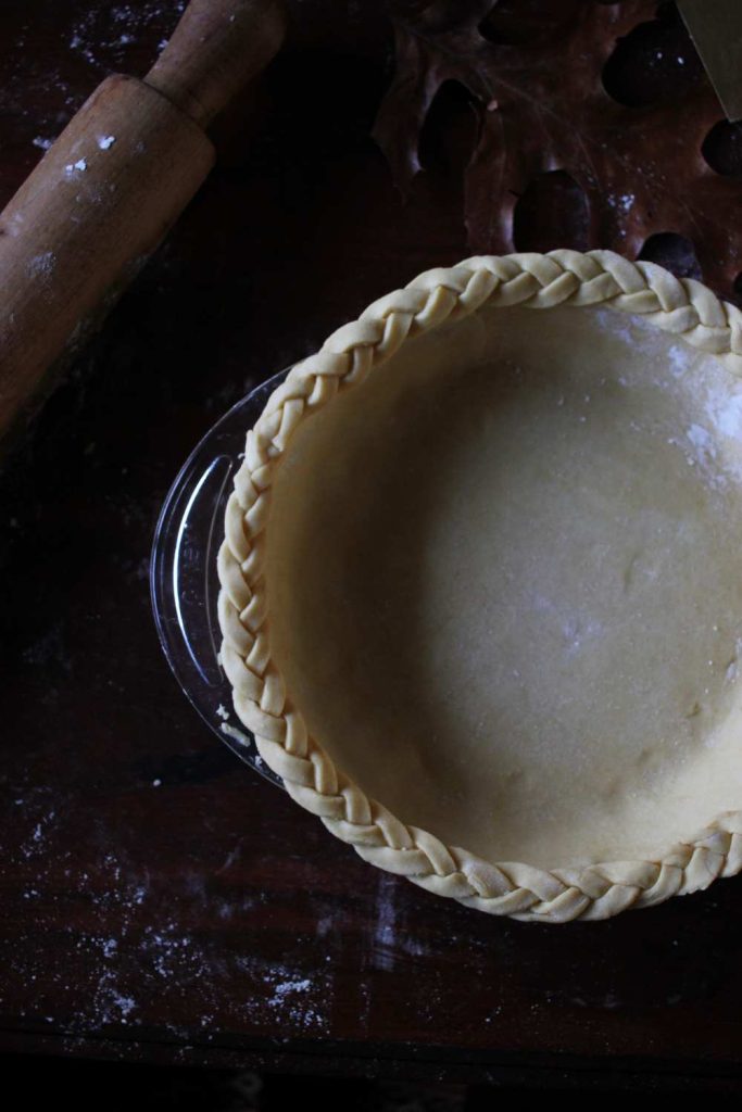 Close up of braided edge of pie crust with wooden rolling pin in upper left corner.