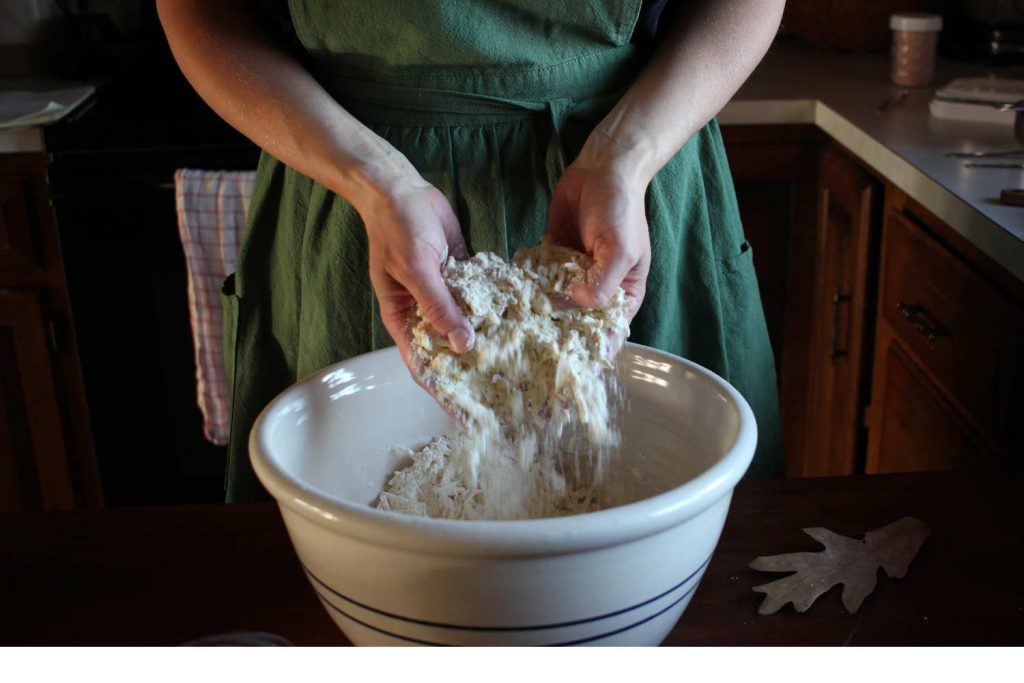 Woman's hands sifting flour, salt and butter mixture through her hands into a large bowl.
