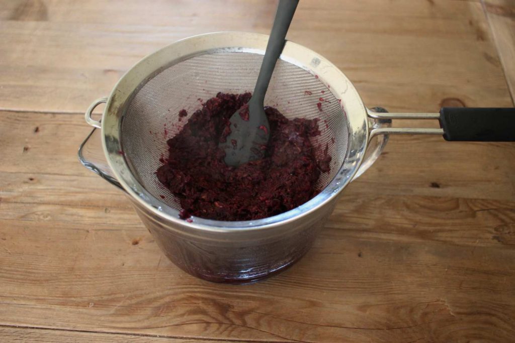 How to make elderberry syrup step 4- strain off berried using a fine mesh strainer press out with a spatula