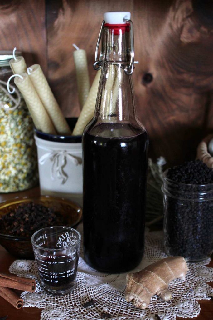 a flip top glass bottle with homemade elderberry syrup surrounded by ingredients and other dried herbs