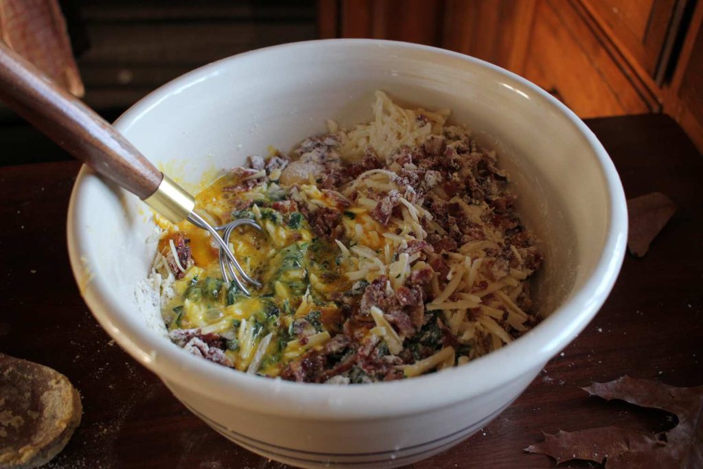 Quiche batter in a large stoneware mixing bowl with a danish whisk.