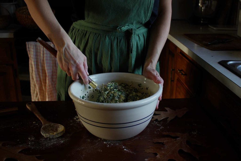 Close up of woman hands stirring a quiche batter in a large stoneware bowl with a whisk.