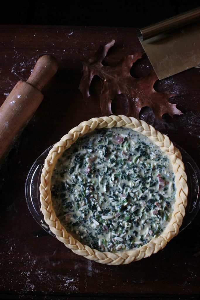 A simple recipe of spinach and bacon quiche in a pie pan with a braided einkorn pie curst uncooked.