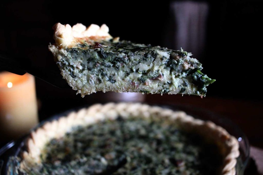Close up photo of a slice of quiche held up on a spatula.
