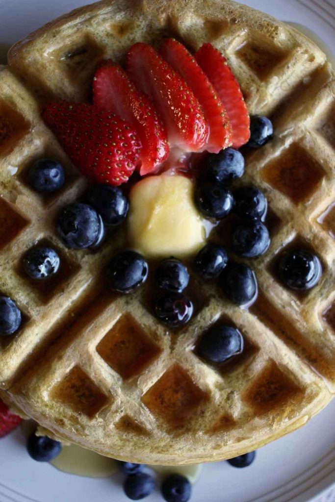 Close of picture of fresh strawberries and blueberries with melted butter on top of sourdough waffles.