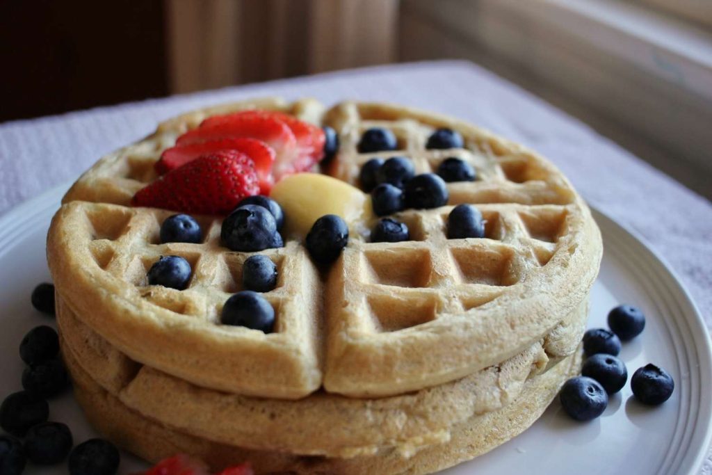 Homemade sourdough waffles stacked on a plate with sliced strawberries and blueberries and melted butter.