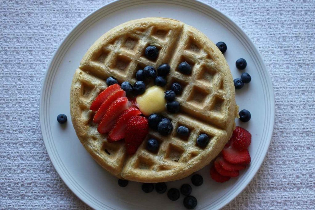 Overhead picture of waffles on a white plate with fresh fruit and melted butter on top.